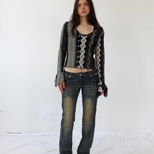 Puede incluir: Una mujer con una camisa de manga larga con estampado blanco y negro con un dobladillo con volantes y pantalones vaqueros azules.