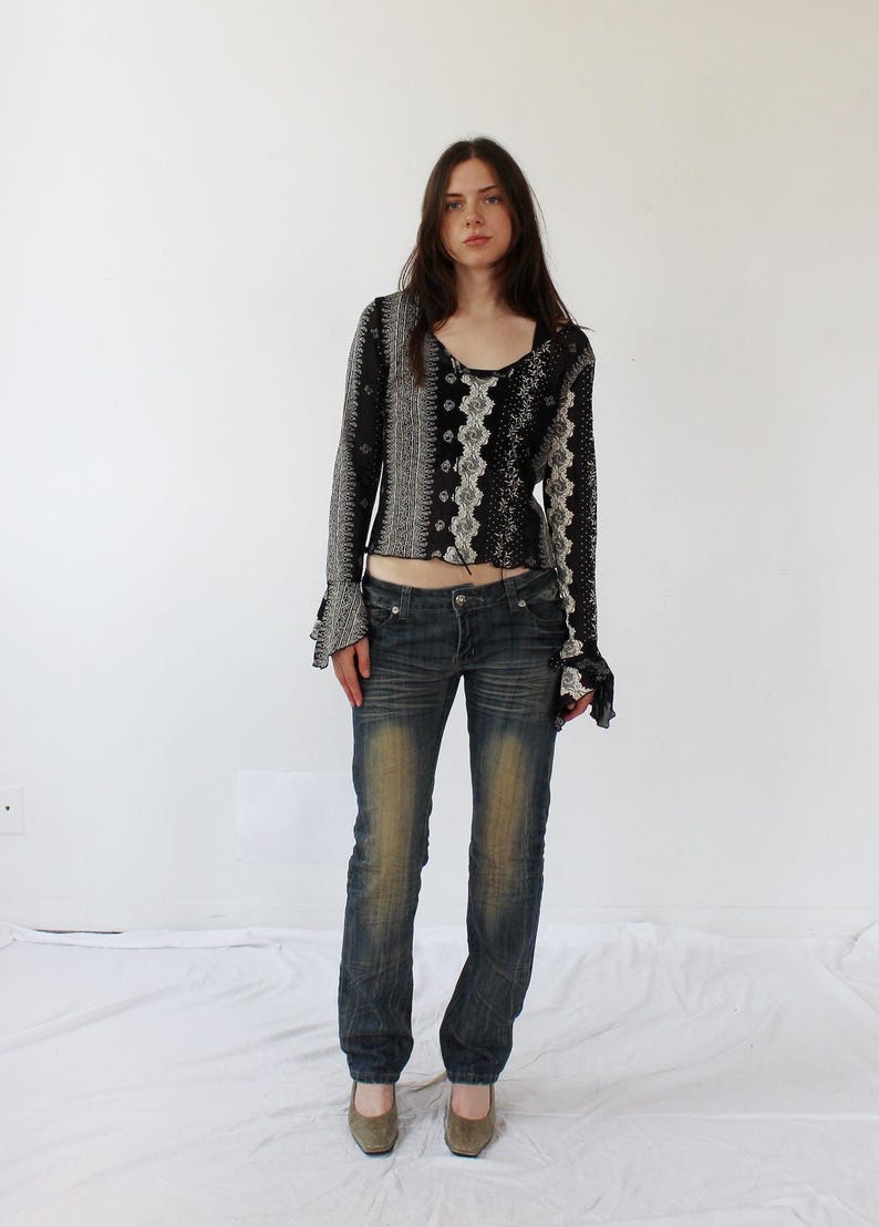 Puede incluir: Una mujer con una camisa de manga larga con estampado blanco y negro con un dobladillo con volantes y pantalones vaqueros azules.