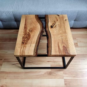 May include: A wooden coffee table with a black metal frame. The table top is made of two pieces of wood with a clear epoxy resin river running through the center.