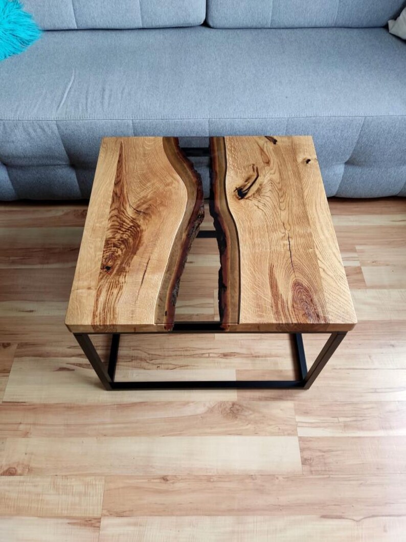 May include: A wooden coffee table with a black metal frame. The table top is made of two pieces of wood with a clear epoxy resin river running through the center.