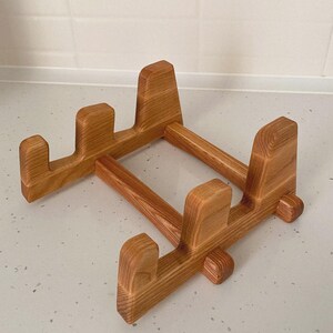 May include: A light brown wooden stand with a rectangular base and four upright supports. The stand is made of natural wood and has a simple, functional design. The stand is likely used to hold a laptop or other electronic device.
