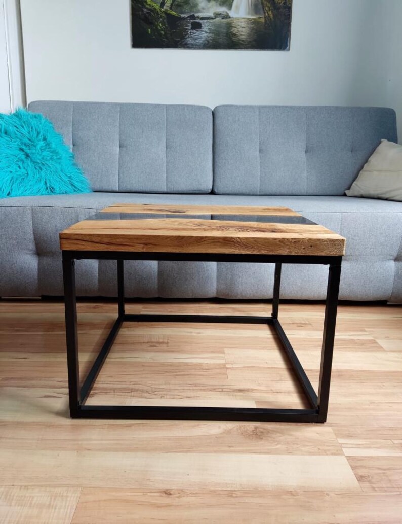 May include: A square coffee table with a wooden top and a black metal frame. The top has a dark gray epoxy river running through the center.