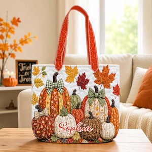 May include: A quilted tote bag featuring a pattern of various pumpkins and autumn leaves in shades of orange, yellow, red, and green. The bag has orange handles and the name Sophia is printed in white script on a central white pumpkin.