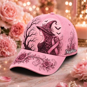 May include: A light pink baseball cap featuring a graphic illustration of a witch in a floral hat, a breast cancer awareness ribbon, bats, and a full moon. The design includes intricate rose patterns and the name Sophia printed in script.