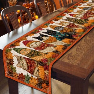 May include: A rectangular table runner featuring a repeating pattern of cats wearing colorful knit hats and scarves, interspersed with orange pumpkins, brown pinecones, and autumn leaves in shades of red, orange, yellow, and green on a white background.