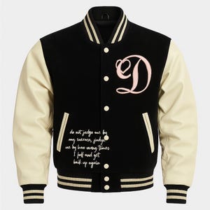 Könnte beinhalten: Schwarze Collegejacke mit cremefarbenen Ärmeln. Sie hat einen großen rosa Buchstaben "D" und weißen Text auf der Vorderseite. Die Jacke hat einen gestreiften Kragen, Bündchen und Saum. Der Text lautet: "Beurteile mich nicht nach meinem Erfolg, beurteile mich danach, wie oft ich gefallen bin und wieder aufgestanden bin."