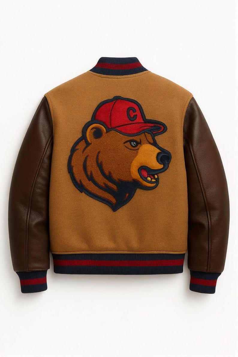 May include: A brown varsity jacket with brown leather sleeves. The back of the jacket features a bear wearing a red baseball cap with a white "C" on it. The jacket has a navy blue, red, and white striped collar, cuffs, and hem.