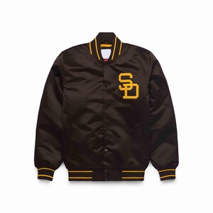 Puede incluir: Chaqueta bomber de satén marrón con cuello, puños y cintura a rayas amarillas y blancas. La chaqueta presenta un gran logotipo "SD" amarillo en el pecho izquierdo. La chaqueta tiene una botonadura.