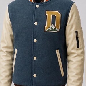 May include: A blue varsity jacket with cream-colored sleeves and a brown collar. The jacket features a large letter "D" patch with a mountain design and a zippered pocket on the sleeve. The jacket has a button-up front and striped cuffs.