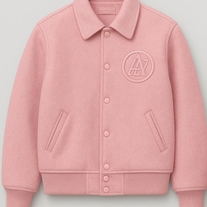 Puede incluir: Chaqueta universitaria rosa claro con cuello, cierre de botones y puños y dobladillo acanalados. Cuenta con un parche circular con un diseño de "A" en el pecho. Dos bolsillos delanteros.