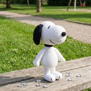 Könnte beinhalten: Handgemachte, weiße Snoopy-Häkelpuppe mit schwarzen Ohren und einer schwarzen Nase. Die Puppe hat einen schwarzen Kragen und steht auf einer Holzbank. Mehrere klare Glassteine ​​sind um die Basis der Puppe verstreut.