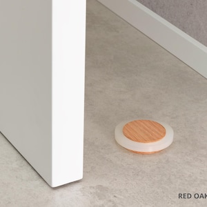May include: A round door stop with a red oak wood center and a clear, rubbery outer ring. The door stop is 0.67 inches in diameter and is on a light gray floor. The text "RED OAK - 16mm &asymp; 0.67" is at the bottom.