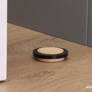 May include: A round, wooden bottle stopper with a black ring and a light wood center. The stopper is approximately 0.63 inches in diameter. The product is labeled "ASH - 16mm &asymp; 0.63".