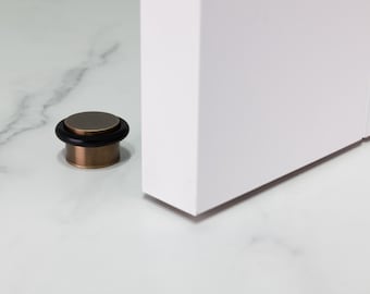 May include: A bronze doorstop with a black rubber stopper. The doorstop is on a white marble floor.