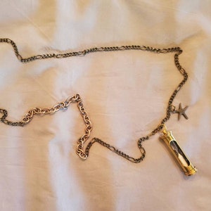 May include: A long necklace with a gold and silver chain. The necklace features a gold hourglass pendant and a small starfish charm. The hourglass has a clear tube with sand inside. The chain is laid out on a white surface.