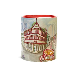May include: A red and white ceramic mug with a watercolor illustration of a street scene in Hong Kong. The illustration features a building with the number 1939 on it, and a cup of tea with a pastry on top. The mug has a red rim.