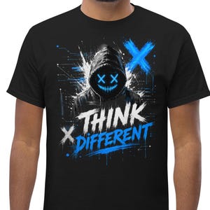 Può includere: T-shirt nera con un design grafico raffigurante una figura incappucciata con dettagli blu e le parole "THINK DIFFERENT". Il design include segni "X" blu e uno sfondo in stile digitale. La maglietta è realizzata in un materiale morbido.