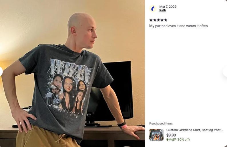 May include: A dark gray short-sleeve crew neck t-shirt featuring a graphic print with the word WIFEY in large metallic-style lettering above a collage of multiple photographs of a person, with small sparkling star accents at the bottom.