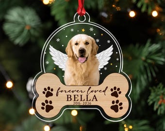 May include: A bone-shaped memorial ornament featuring a golden retriever with white angel wings against a black background with stars and snowflakes. The wood-toned base displays the text forever loved BELLA 2015-2026 and four black paw prints.