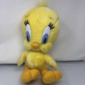 May include: A plush yellow Tweety Bird toy with large blue eyes, black eyelashes, and an orange beak. The stuffed animal has yellow feet and a tuft of yellow feathers on top of its head. The toy is a classic cartoon character.