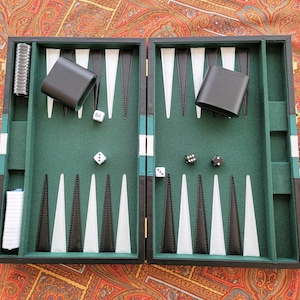 May include: Open backgammon board with a green playing surface, black and white triangles, and black leather dice cups. The board is open, displaying dice and game pieces. The game is set on a patterned fabric background.
