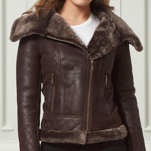 May include: A brown leather jacket with a shearling collar and trim. The jacket has a zip-up front, two zippered pockets, and quilted detailing on the sleeves. The jacket is worn over a white t-shirt.