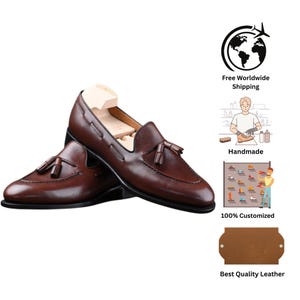 May include: A pair of brown leather loafers with tassel detailing. The shoes have a classic design with a pointed toe and a low heel. The image also includes a shoe tree inside one of the shoes.
