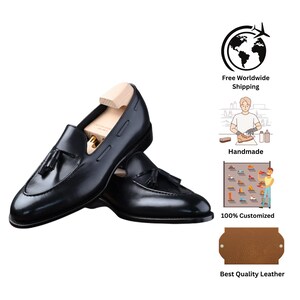 May include: A pair of black leather loafers with tassel detailing. The shoes are displayed with wooden shoe trees inside, showcasing their shape and structure. The design features a classic, polished finish.