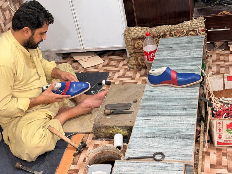 May include: A blue and red leather shoe on a wooden last, featuring a sleek design with a pointed toe. The shoe is constructed with vibrant blue panels accented by a bold red stripe along the side, showcasing precise stitching and a smooth finish.