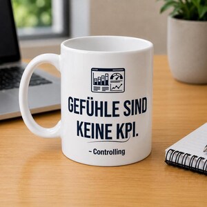 May include: A white ceramic mug featuring a dark blue graphic of a data dashboard icon above the text "GEFÜHLE SIND KEINE KPI." and "- Controlling" printed in a bold, sans-serif font on the front surface of the cylindrical drinking vessel.