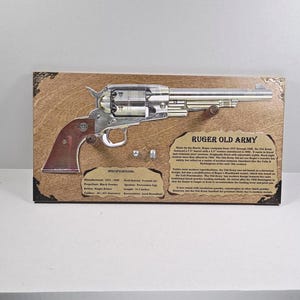 May include: A framed display featuring a Ruger Old Army revolver. The firearm is silver with a brown grip, mounted on a wooden plaque with text. The plaque includes specifications and historical information about the revolver.