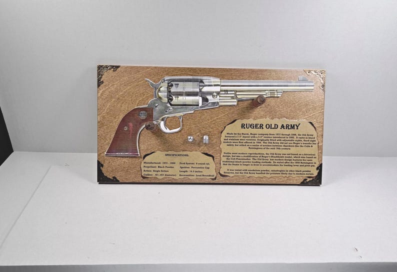 May include: A framed display featuring a Ruger Old Army revolver. The firearm is silver with a brown grip, mounted on a wooden plaque with text. The plaque includes specifications and historical information about the revolver.