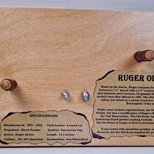May include: Wooden display featuring a Ruger Old Army firearm. The display includes text with specifications, a description, and two lead roundballs. The firearm's barrel length is 14.5 inches.