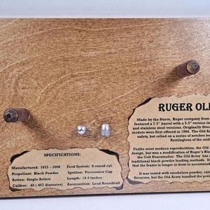 May include: Wooden display featuring a Ruger Old Army firearm. The display includes text with specifications and historical details. The barrel length is 14.3 inches. Decorative metal corner accents.
