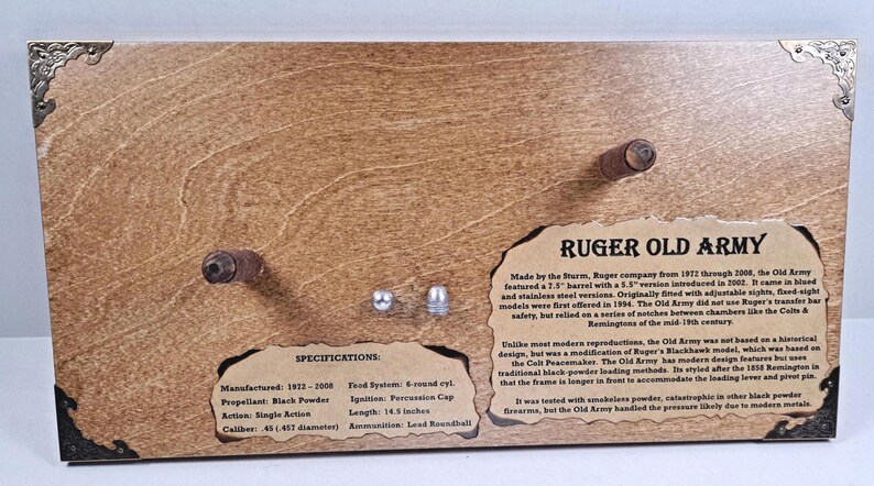 May include: Wooden display featuring a Ruger Old Army firearm. The display includes text with specifications and historical details. The barrel length is 14.3 inches. Decorative metal corner accents.