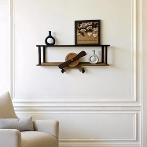 Może przedstawiać: Wnętrze pokoju z kremowym fotelem i szarą poduszką. Drewniana półka prezentuje dekoracyjny samolot, wazony i oprawione dzieło sztuki. Biała ściana ma listwy, a dywan pokrywa podłogę.