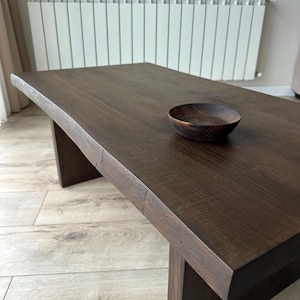 Puede incluir: Una mesa de centro de madera marrón oscuro con un cuenco de madera a juego. La mesa tiene una parte superior rectangular y una base robusta. El cuenco es redondo y se encuentra sobre la superficie de la mesa. La mesa mide unos 122 cm de largo.