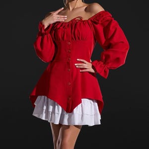 May include: A red off-the-shoulder top with long sleeves and a button-down front. The top is paired with a white, ruffled skirt. The sleeves have a ruffled cuff. The outfit is a combination of a blouse and skirt.