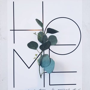 May include: A black and white print with the words "sweet home" written in cursive. The word "home" is formed with geometric shapes and a sprig of green eucalyptus is placed in the center of the print.