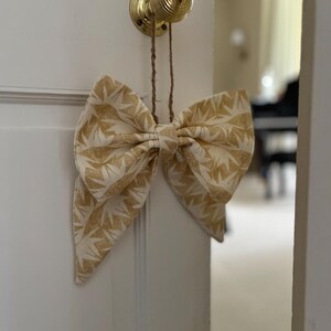 May include: A large, cream-coloured fabric bow with a gold geometric pattern hangs from a brass door knob.