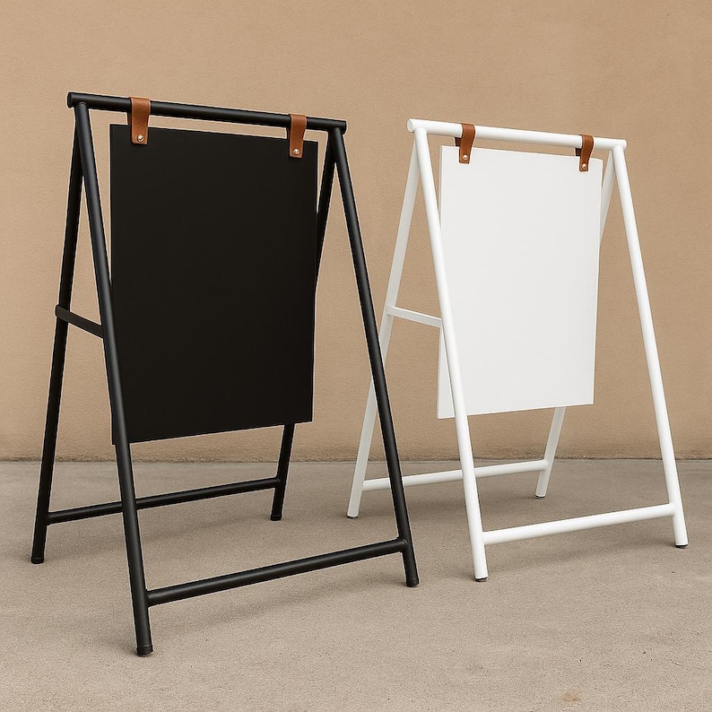May include: Two metal A-frame signs, one black and one white, with rectangular panels. The signs have a minimalist design with brown leather straps at the top. The black sign is on the left, and the white sign is on the right.