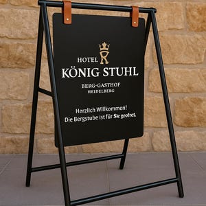 May include: Black metal A-frame sign with the text "HOTEL K&Ouml;NIG STUHL" in gold lettering. The sign also includes the text "BERG-GASTHOF HEIDELBERG" and a welcome message. The sign is held by brown leather straps.