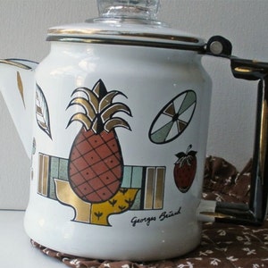 May include: White enamel coffee pot with a black handle and gold trim. The pot features a colorful fruit design, including a pineapple, strawberry, and other geometric shapes. The words "Georges Briard" are printed on the side.