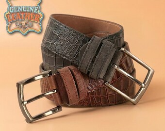 Può includere: Due cinture in pelle con fibbie argentate. Una è marrone scuro con motivo a coccodrillo, l'altra marrone chiaro con texture scamosciata. L'immagine include un emblema "GENUINE LEATHER".