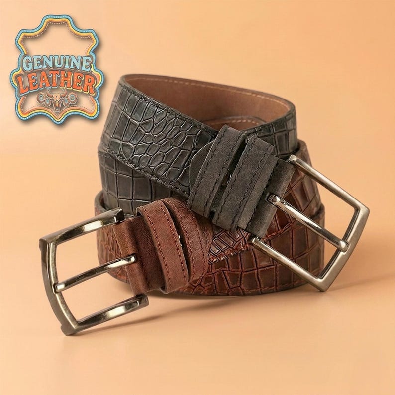 Pu&ograve; includere: Due cinture in pelle con fibbie argentate. Una &egrave; grigio scuro con motivo a coccodrillo, l'altra marrone. Le cinture sono etichettate "GENUINE LEATHER" in un emblema decorativo.