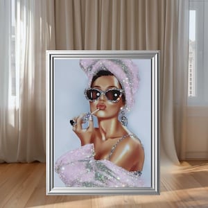 May include: Framed artwork featuring a glamorous woman in a pink towel, sunglasses, and jewelry. The image has a silver frame and is set against a neutral background. The woman is holding a cigarette and has red lipstick.