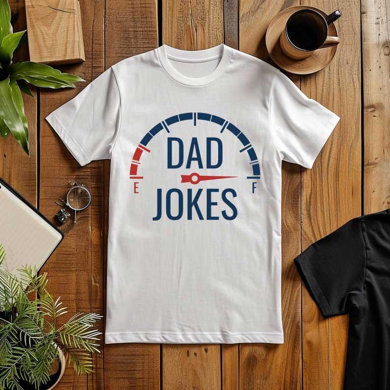 May include: White t-shirt with a blue and red graphic that reads "DAD JOKES". The design resembles a fuel gauge, with "E" and "F" on either side. The shirt is displayed on a wooden surface.