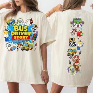 May include: An off-white t-shirt featuring a graphic print on the front and back. The front displays a yellow school bus, a rocket, a cowboy hat, and the text "BUS DRIVER STORY TO INFINITY AND BEYOND FOR OUR STUDENTS". The back shows a vertical arrangement of school and character-themed icons including a backpack, apple, vest, and bus.