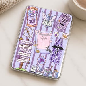 May include: A clear phone case with a purple and white striped background, decorated with fantasy-themed stickers. The stickers include dragons, swords, a soda can, and text that reads "Fantasy Reader Soda" and "Girlie".