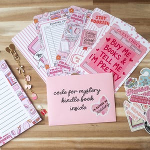 Pode incluir: Uma coleção de artigos de papelaria rosa e brancos, incluindo um bloco de notas, registros de leitura, adesivos e um envelope com texto. Os itens têm um tema de livros com frases como "Buy Me Books & Tell Me I'm Pretty."